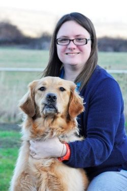 Amy is smiling at the camera. She is sitting with a golden retriever.